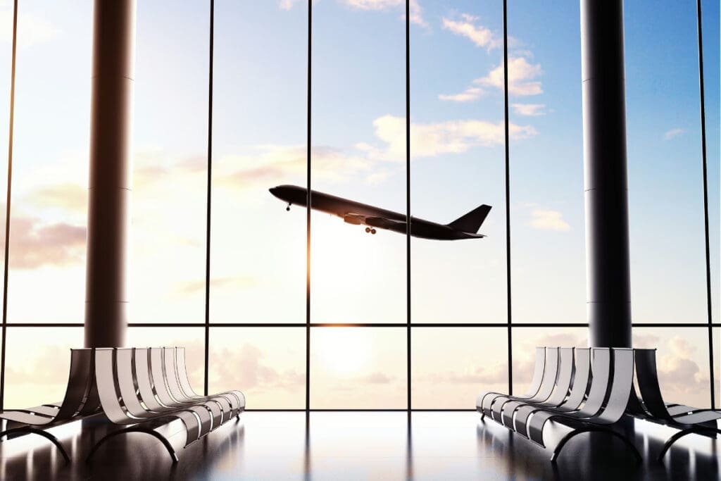 Silhouette of an airplane taking off against a large window in an airport terminal.