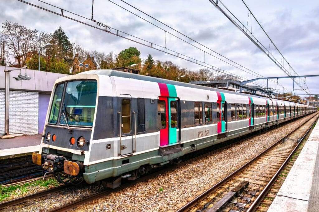 How to Get to Paris from Charles de Gaulle Airport,A train with a white and colorful design parked at a station platform on railway tracks.