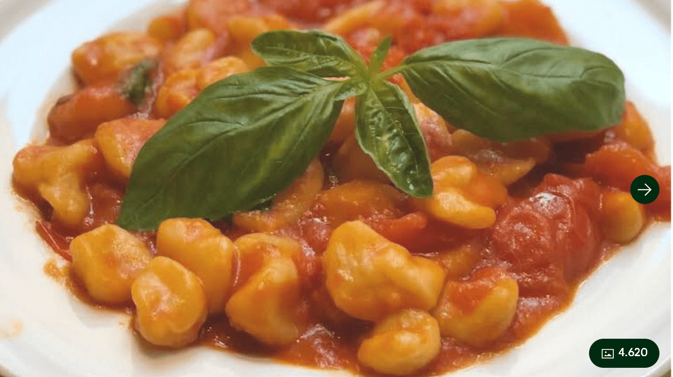 A plate of gnocchi served with tomato sauce and topped with fresh basil leaves.