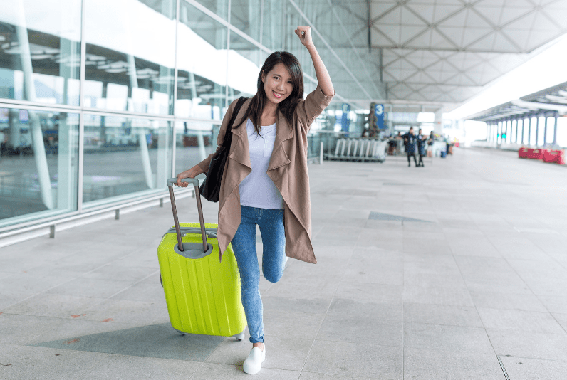 Best Travel Loyalty Programs, A woman in casual attire holding a green suitcase while walking at an airport terminal.