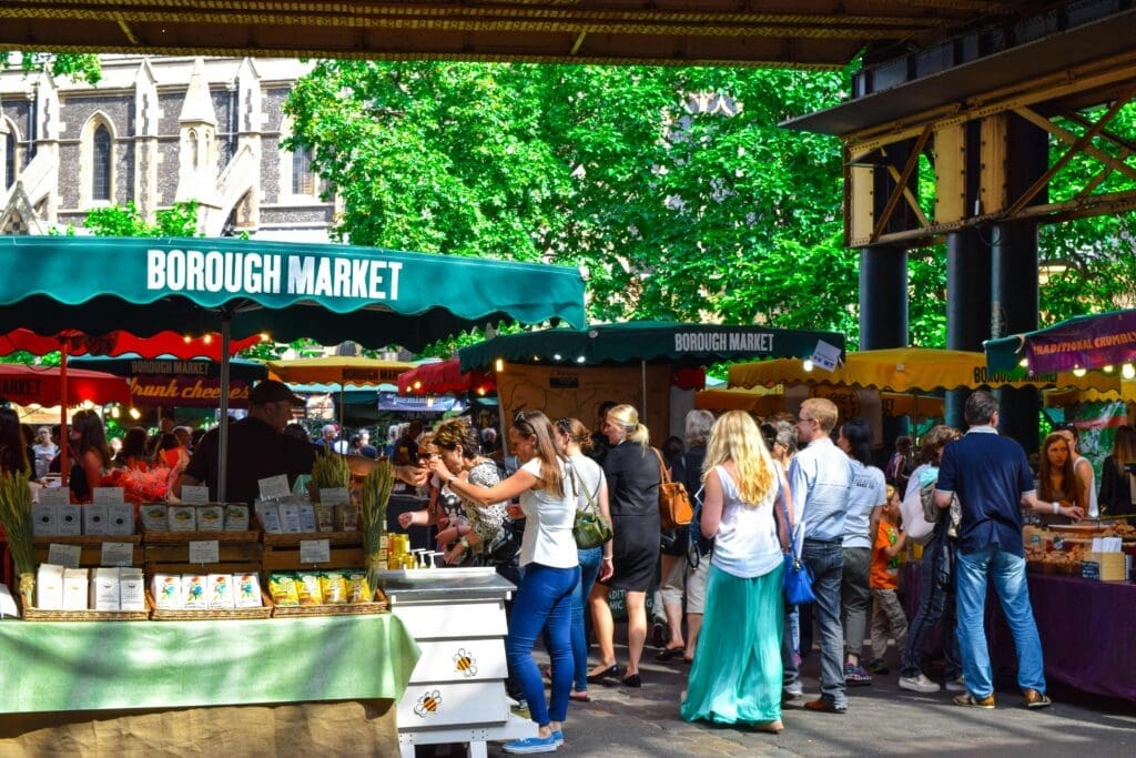 best place for street food in london, View of Borough Market featuring various stalls and visitors browsing the offerings under green canopies.