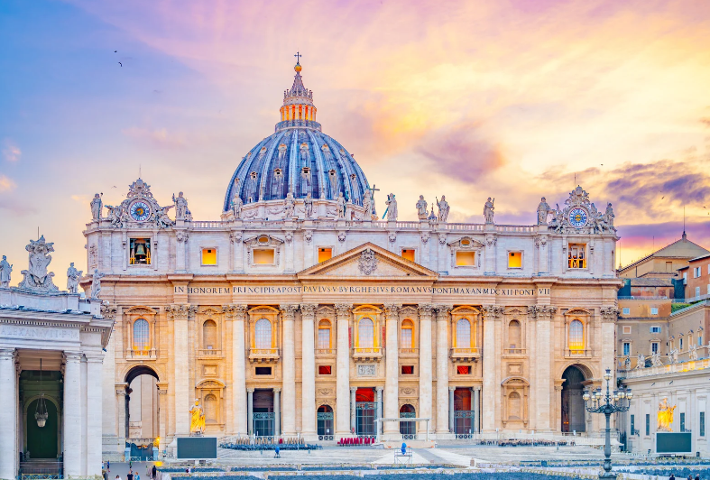 St. Peter’s Basilica in Vatican City at sunset, with a vibrant sky, ornate architecture, large dome, columns, and people gathered in St. Peter’s Square—one of the renowned UNESCO World Heritage Sites in Italy.