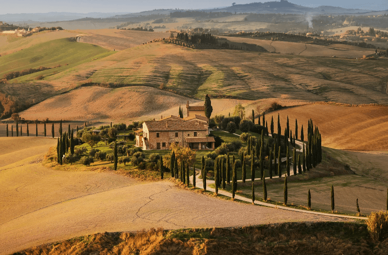 A rustic villa surrounded by cypress trees sits in the middle of rolling golden hills, reminiscent of landscapes found among UNESCO World Heritage Sites in Italy, with winding roads and distant fields under a soft, warm light.
