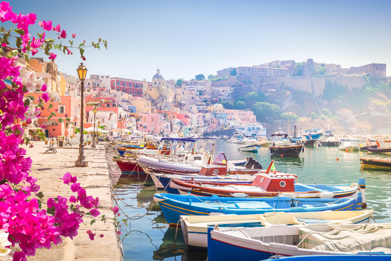 Hidden Gems in Italy, A row of colorful boats docked in a harbor with buildings and flowers in the background.