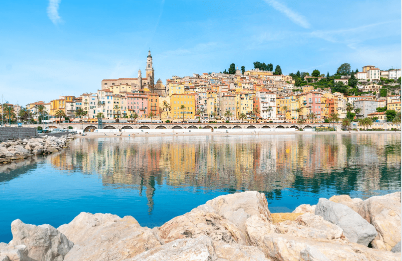 A coastal town featuring colorful buildings reflected in calm water under a clear blue sky.