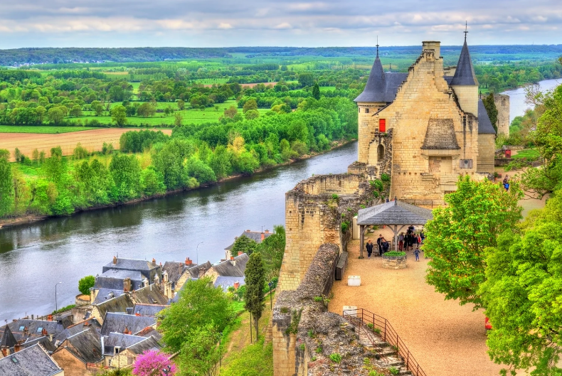 Hidden Gems in France,Stone château with towers situated on a cliff overlooking a river and green landscape.