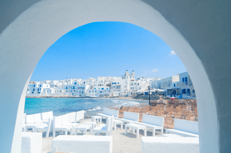 View of white buildings along the coastline with blue water visible through an archway.Hidden gems in Greece 