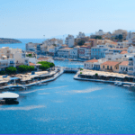 Coastal view of a harbor with boats and buildings lining the waterfront in a Mediterranean setting.